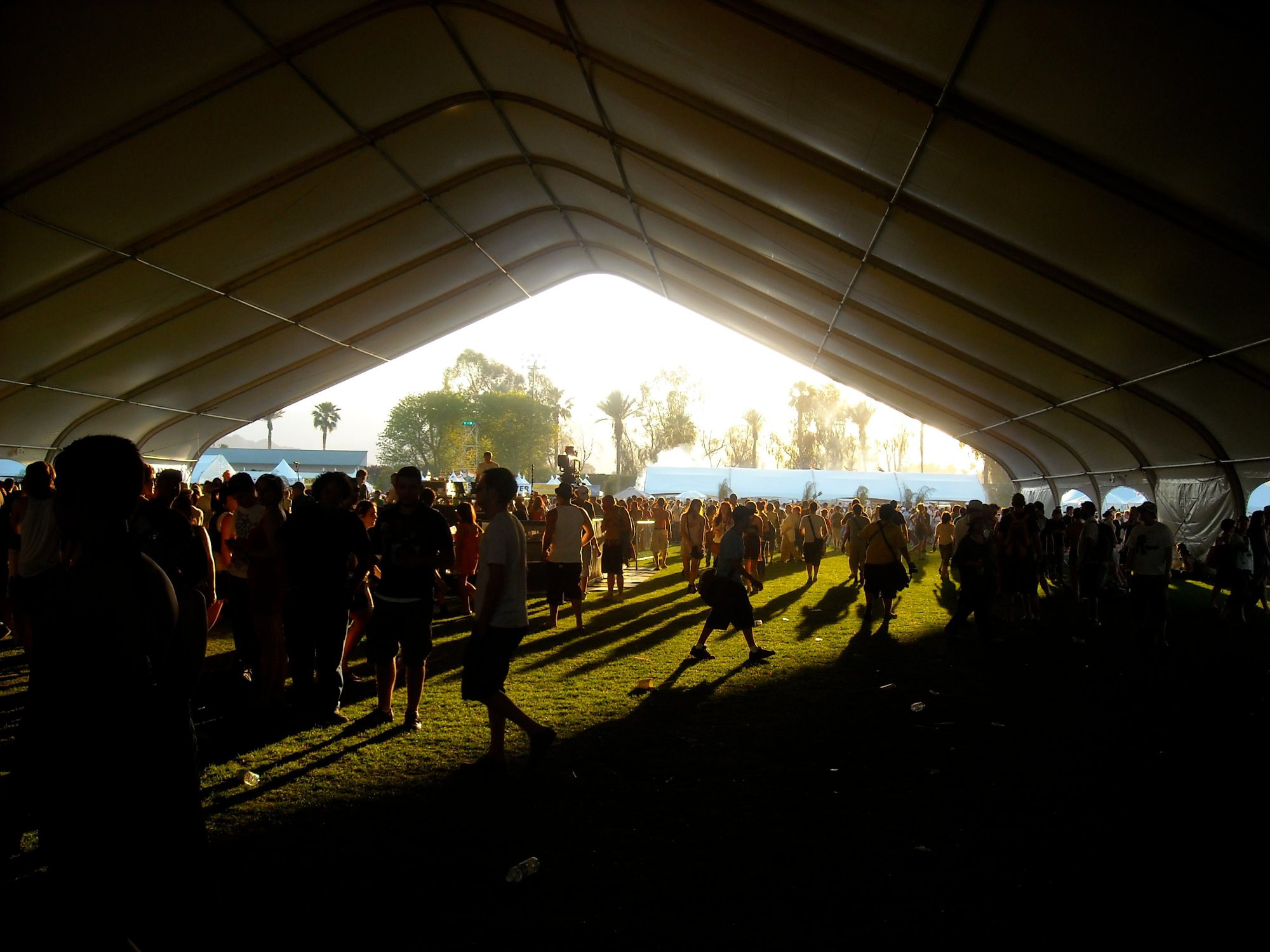 Crowd inside a festival tent, golden afternoon light flooding through the opening